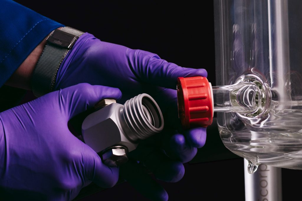 A close up photograph of a chemist attaching an oil pipe to an Orb Jacketed Reactor glass vessel